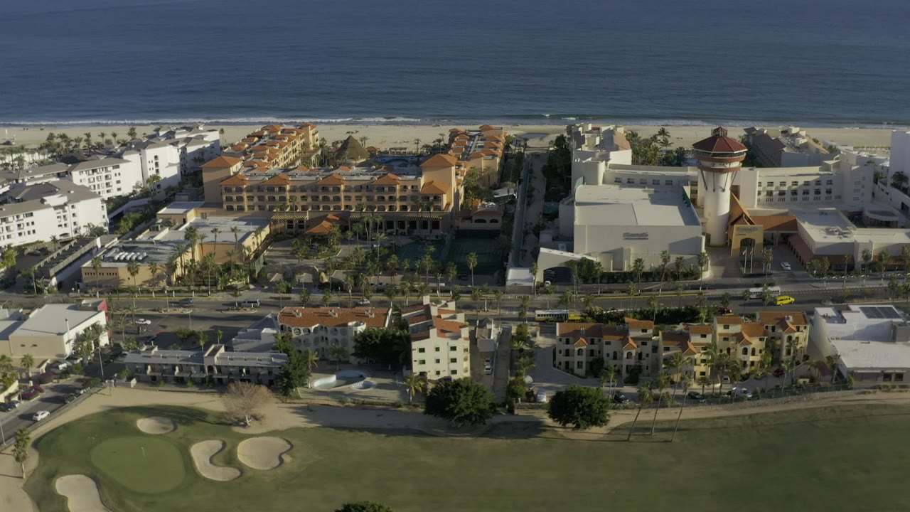 Aerial view of coastal buildings, road, golf green, beach, and ocean.