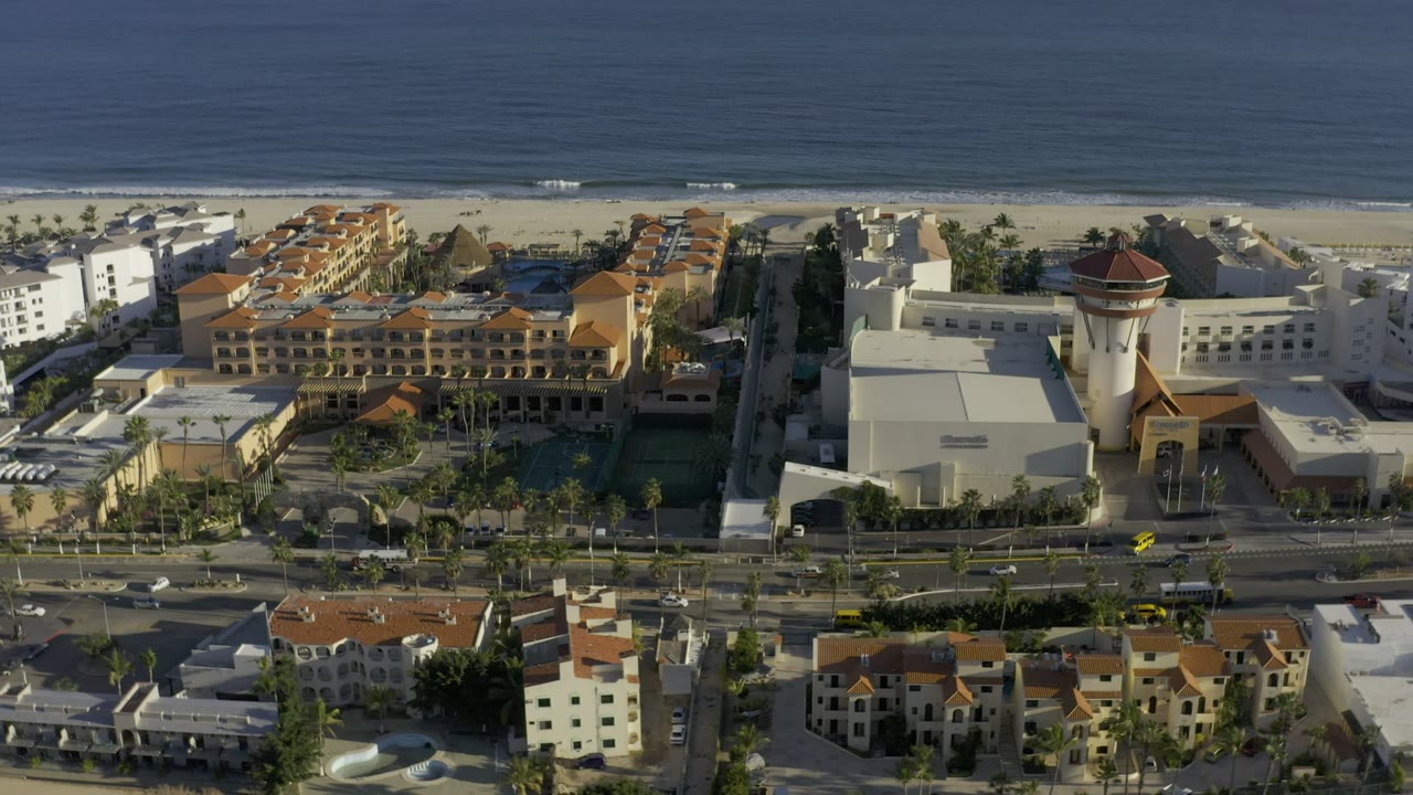 Aerial view of beachfront resort buildings, road traffic, beach, and ocean.