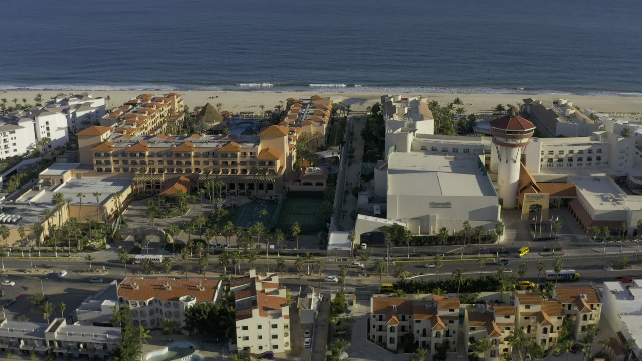 Los Cabos aerial view centered on a large resort complex with orange roofs, pale beachfront buildings, the beach and ocean beyond, and no visible people.