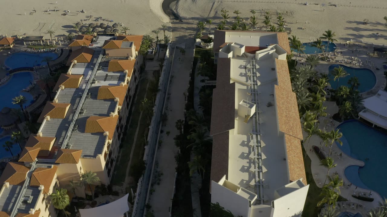 Aerial view of beachfront condos, pools, palms, sand, and shoreline.