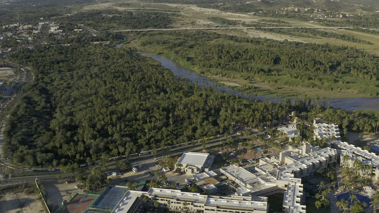 Aerial view of white buildings beside green wetlands and sandy beach.