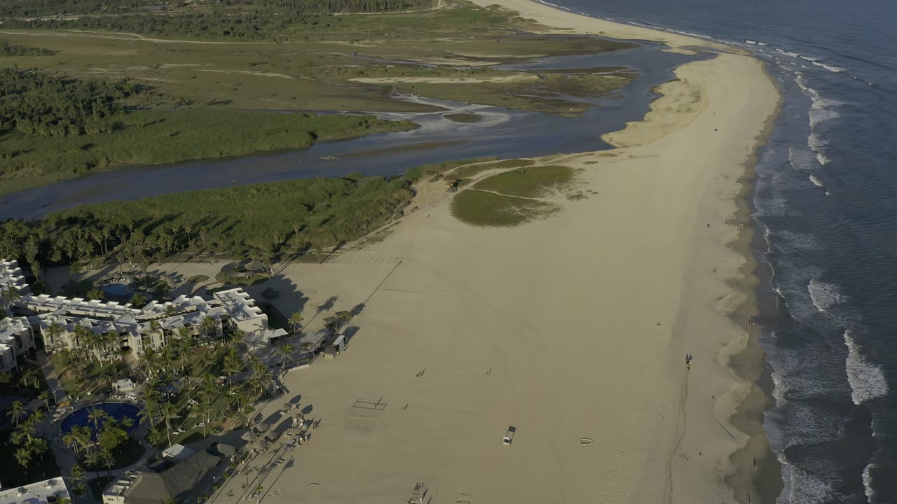 Aerial view of sandy beach, river channel, ocean surf, and coastal buildings.