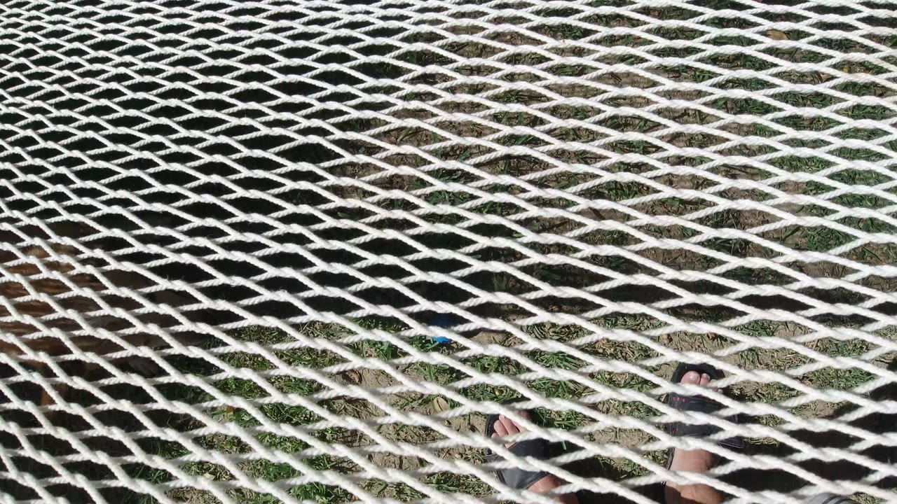 The net appears stretched diagonally across the frame in San Jose del Cabo, Mexico, with grass and dirt visible through the rope openings.