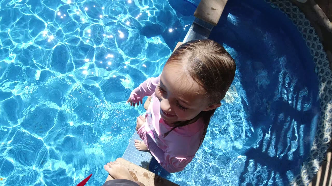 Young child in a pink swim shirt at the edge of a bright blue pool.