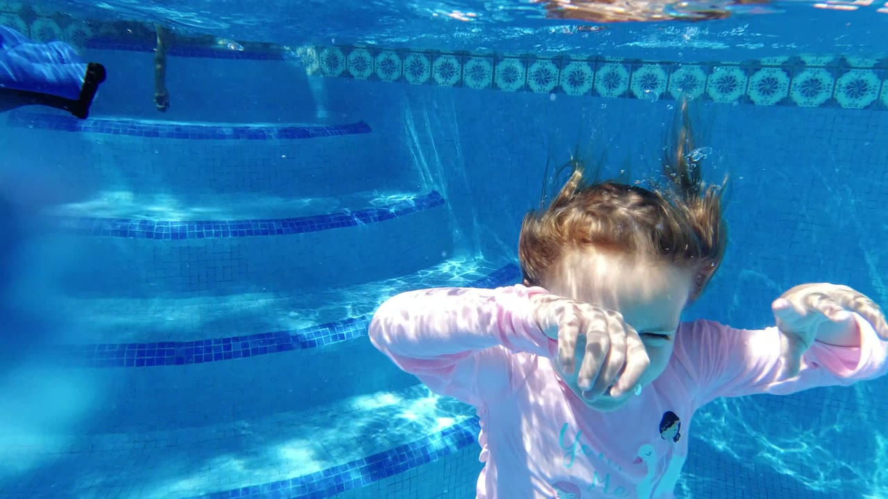 Child underwater in a blue swimming pool with arms forward.