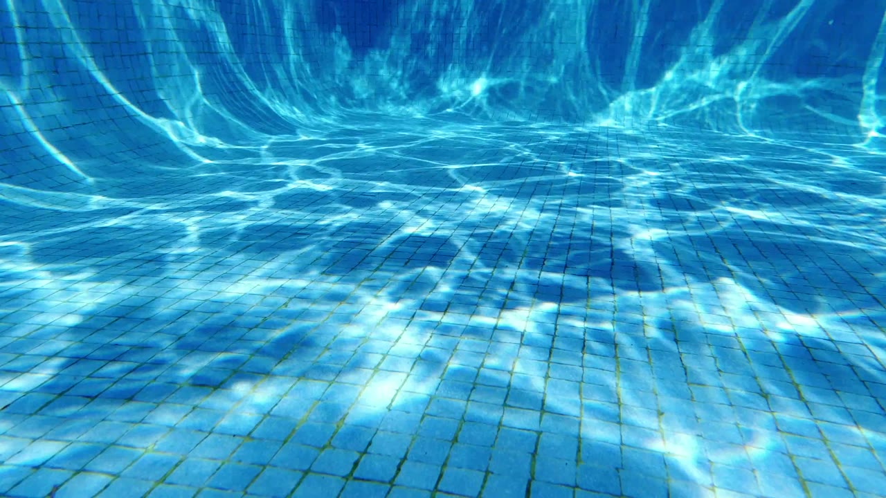 Blue tiled swimming pool floor with sunlight ripples and no visible people.
