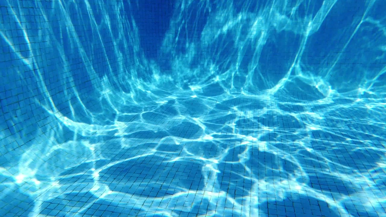 Blue tiled pool corner in San Jose Del Cabo, Mexico, with light refraction spreading over the wall, floor, and step-like ledge, with no visible people.