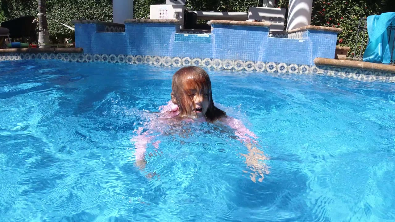 Child in a pink top standing chest-deep in a bright blue pool.