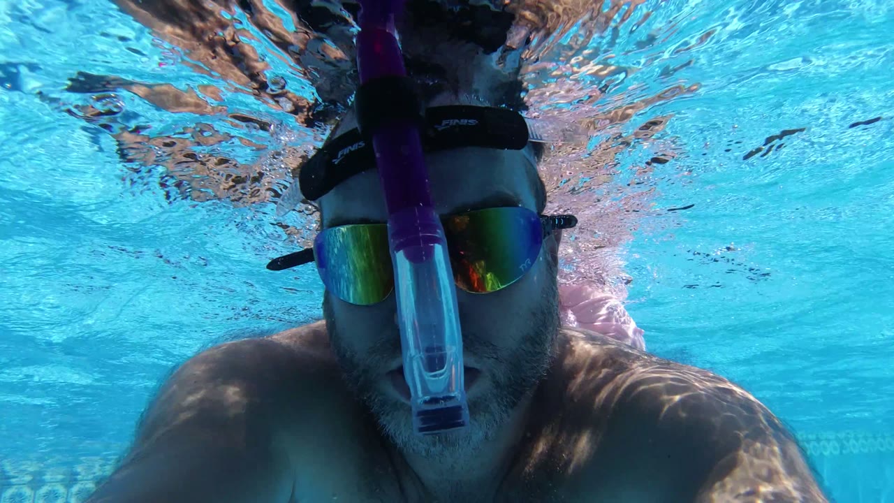 Man underwater in a swimming pool wearing a snorkel mask and reflective goggles.