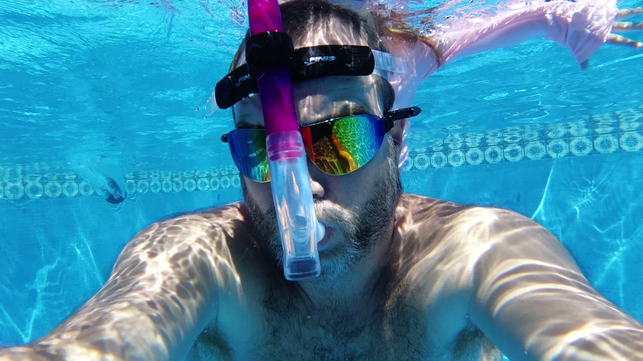 Man underwater in a pool wearing a snorkel mask and mirrored lenses.