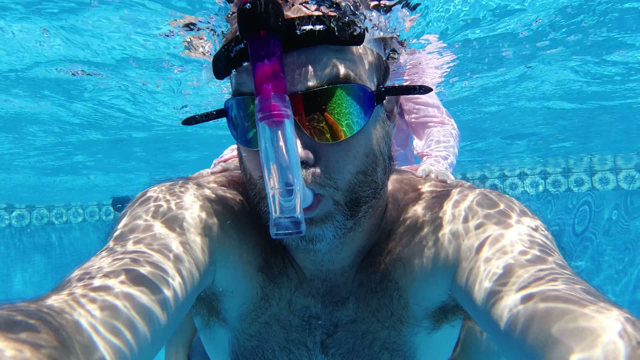 One second in, the man remains centered underwater in San Jose del Cabo, with his arms reaching forward and the pool wall pattern visible behind his shoulders.