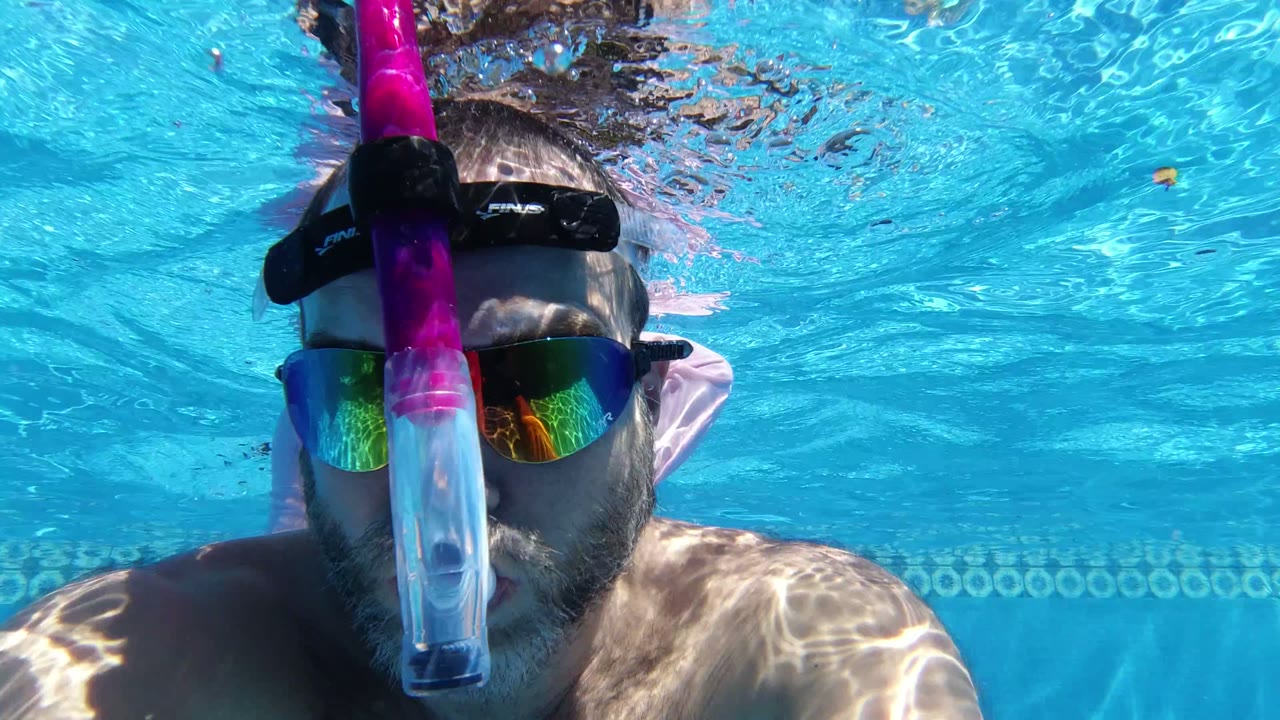 Middle-aged man underwater in a blue swimming pool wearing a snorkel mask.