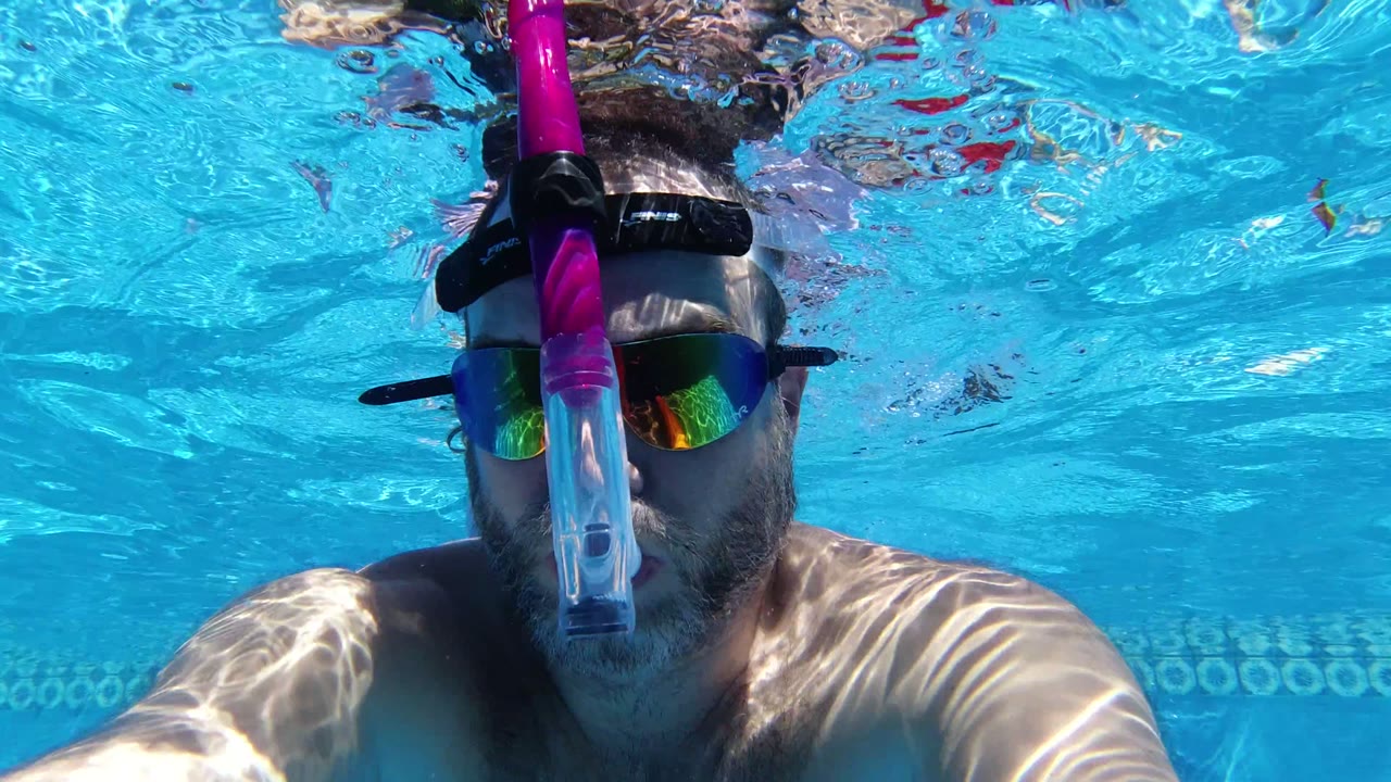 Close underwater frame of the snorkeler in San Jose del Cabo, with his face centered, mirrored lenses visible, and the pool tile band running behind him.