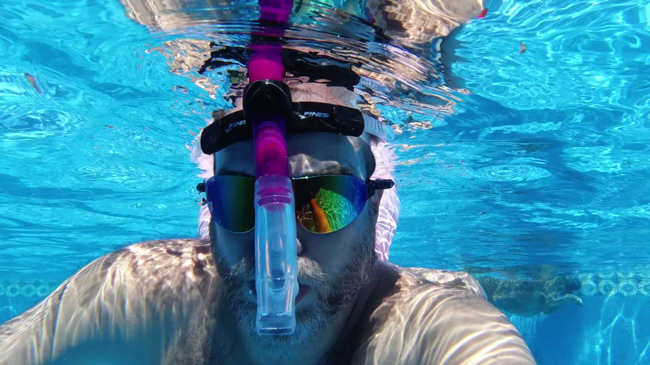 The man remains centered underwater in San Jose Del Cabo, Mexico, with the pink breathing tube vertical in front of his face and sunlight wavering across the pool.