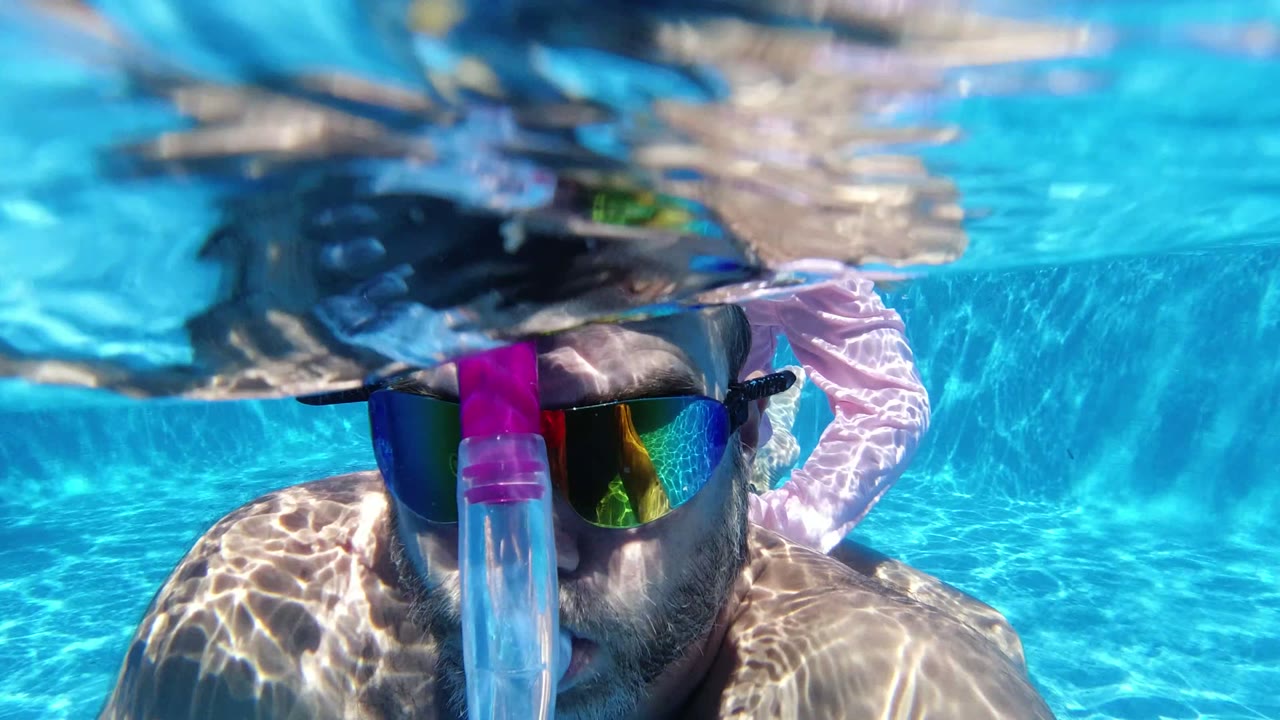 Close waterline view in San Jose del Cabo, Mexico, with an adult man in a snorkel mask partly submerged as ripples distort the top of the frame.