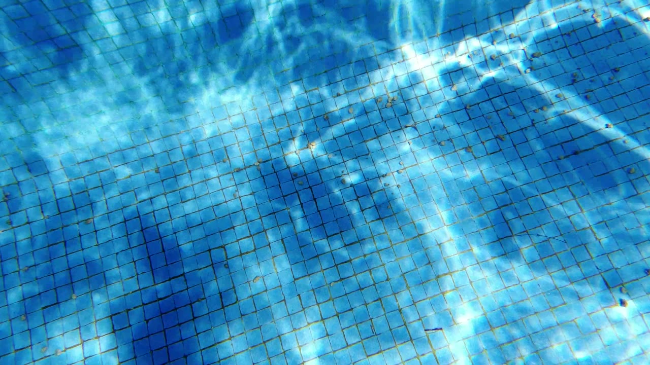 Blue square-tiled pool floor in San Jose del Cabo with bright white sunlight reflections spreading across the water and no visible people.