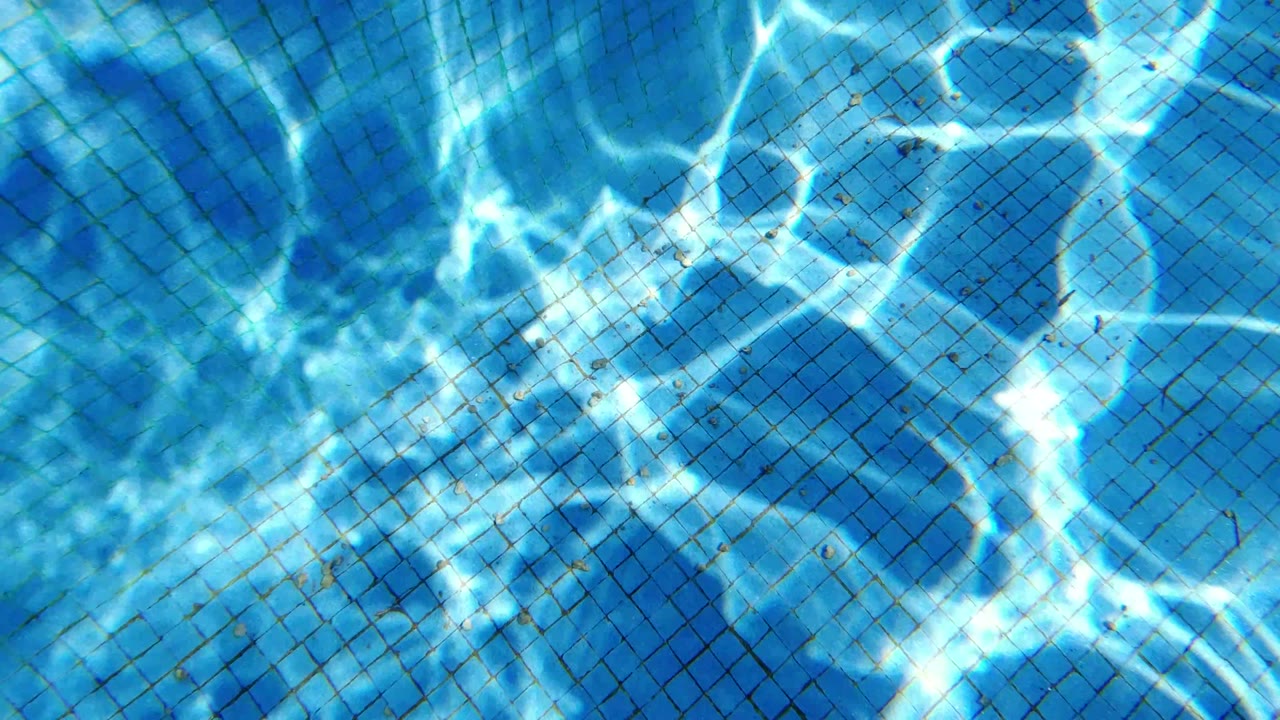 Curved pool wall and blue tile grid in San Jose del Cabo are crossed by bright rippling reflection lines, with no visible people.