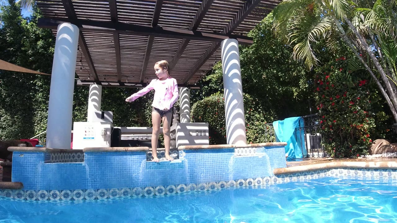 Child standing on a blue tiled pool ledge beside bright water.