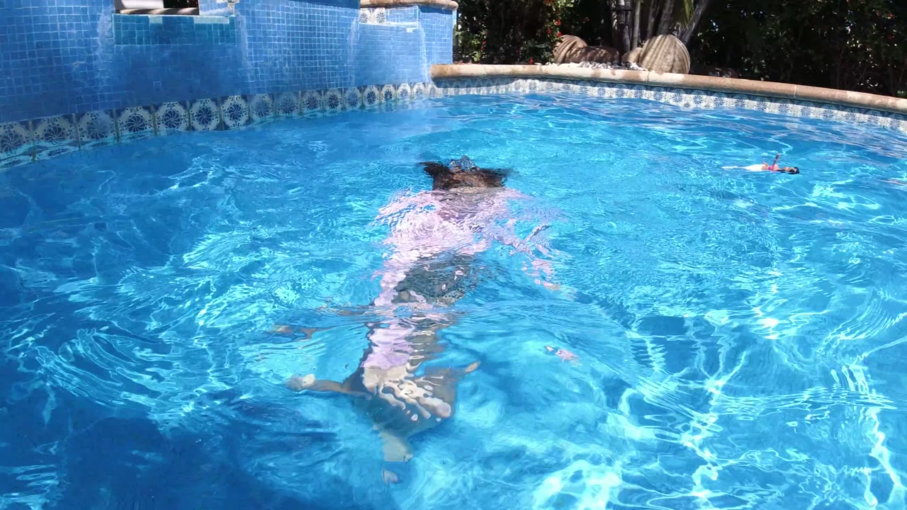 The child swims away from the camera with her head partly submerged in the bright blue pool at the San Jose del Cabo location.