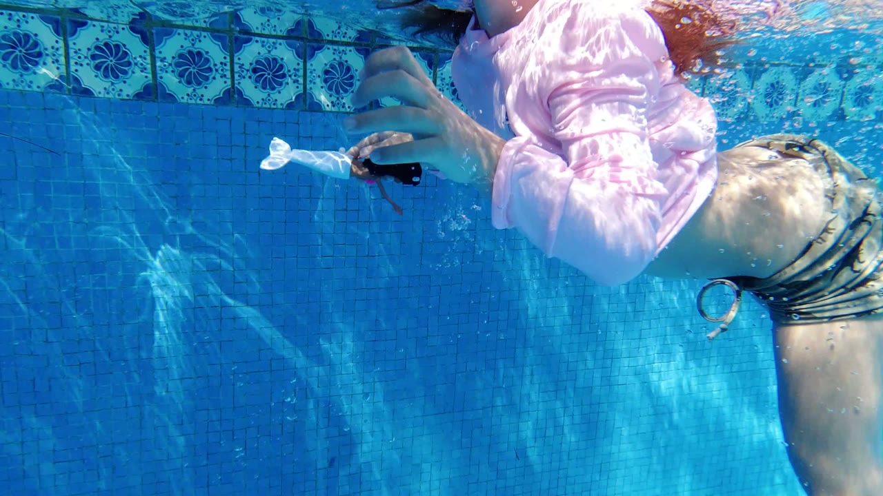 Girl swimming underwater beside blue pool tiles.