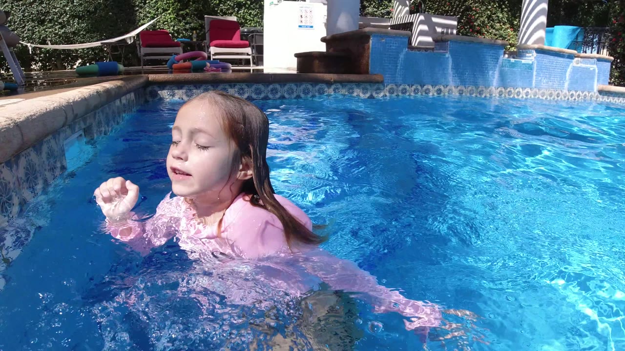 The girl turns sideways with her eyes closed as one hand rises above the rippled pool surface in San Jose del Cabo, Mexico.