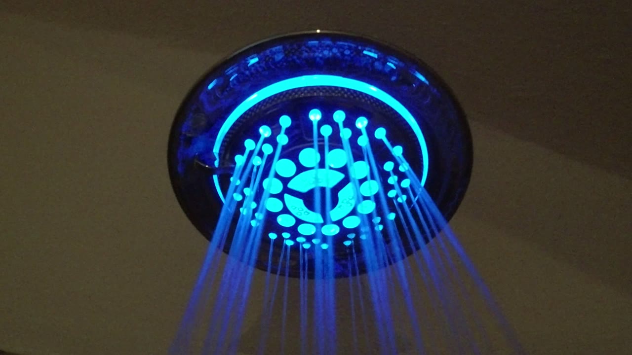 Upward view of a blue neon-lit shower head with water streams falling toward the camera in San Jose del Cabo, Mexico, with no visible people.