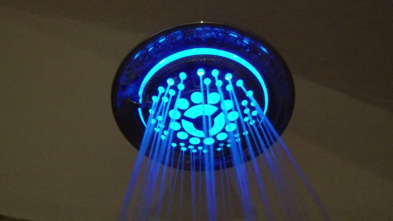 Close upward frame of a cyan and blue shower fixture with parallel water streams against a dim ceiling in San Jose del Cabo, Mexico, with no visible people.