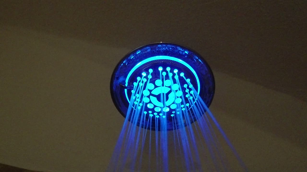 At 0:00 in San Jose del Cabo, Mexico, a round shower head glows blue as thin streams of water spray downward, with no visible people.