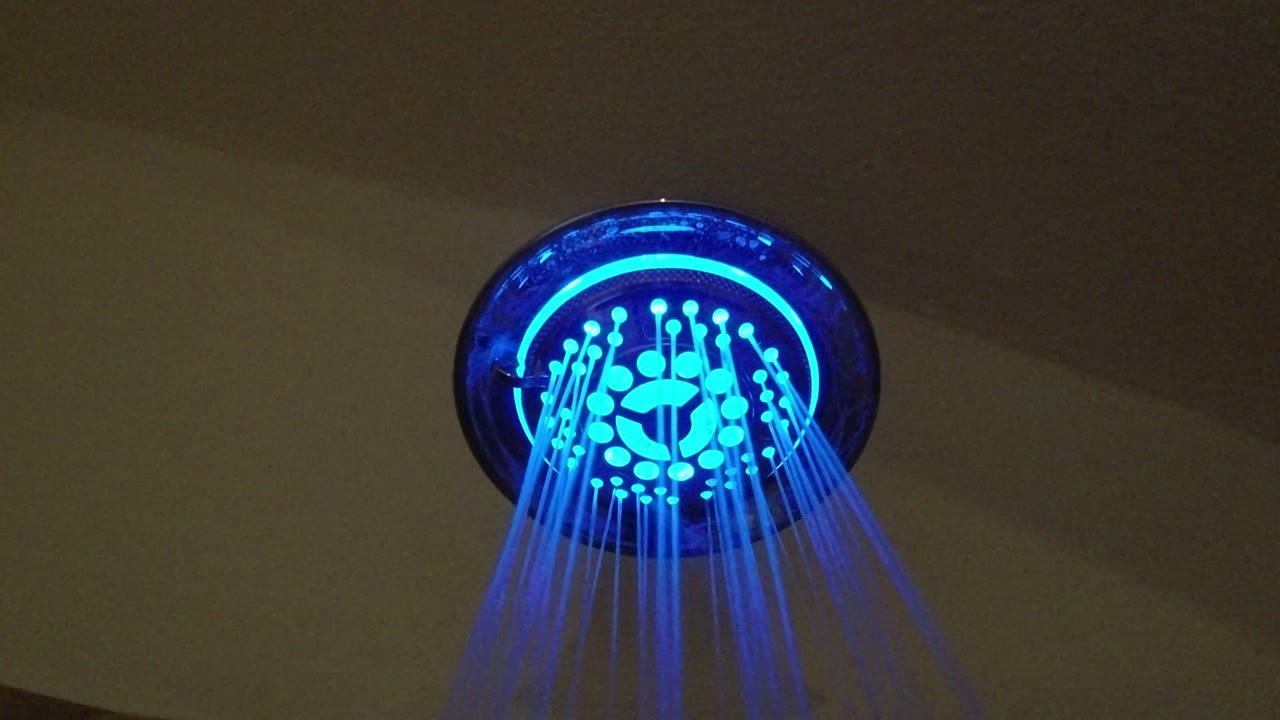 At 0:01 in San Jose del Cabo, Mexico, the blue shower head remains centered high in frame as water lines fall in a narrow fan, with no visible people.
