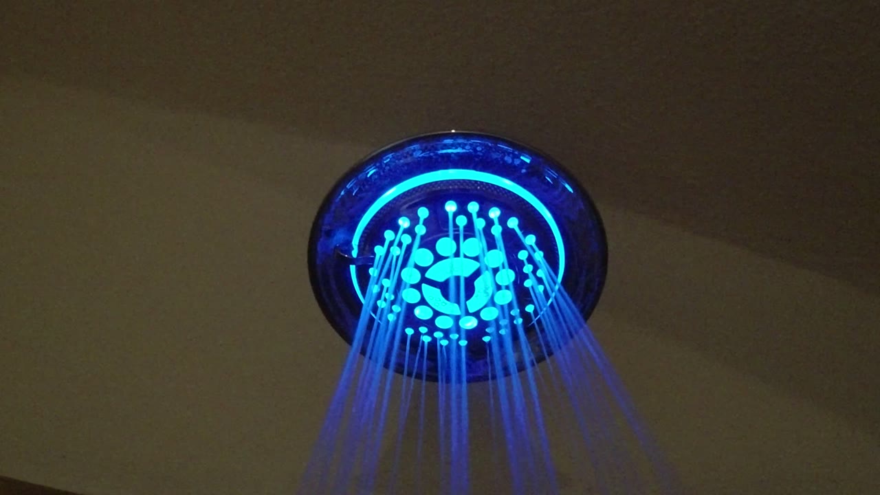 Blue-lit shower head spraying water against a dark ceiling.