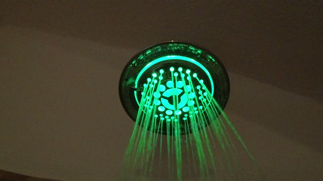 Green LED showerhead spraying water in a dark bathroom