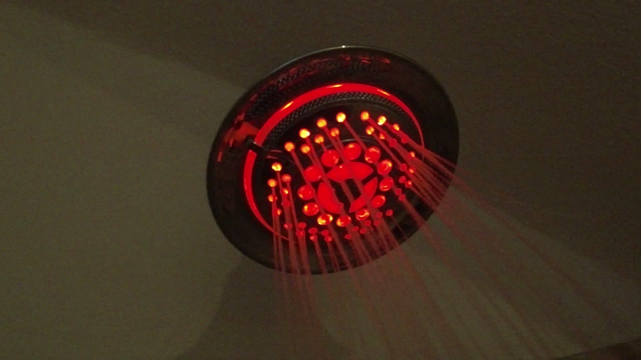 Red-lit round shower head spraying water against a plain wall.