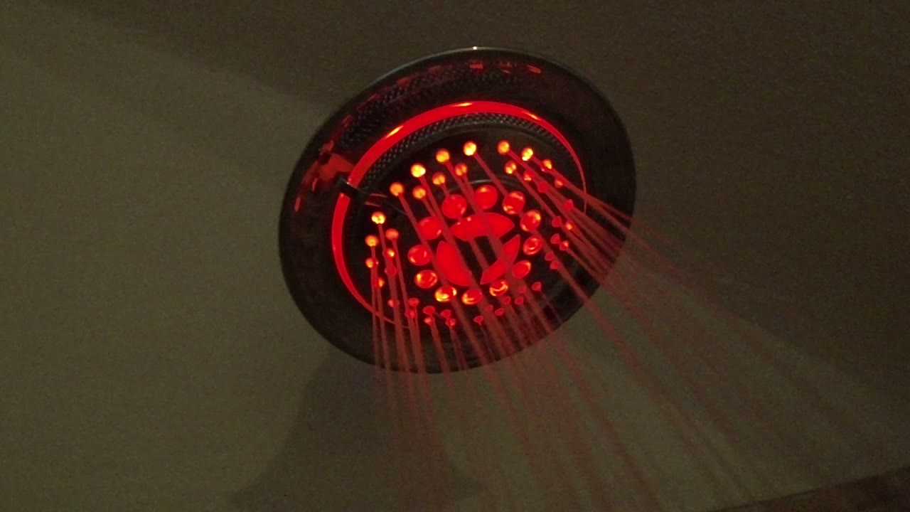 One second in, the shower fixture remains close in frame with red lights reflecting through the falling water, no visible people in the bathroom view.
