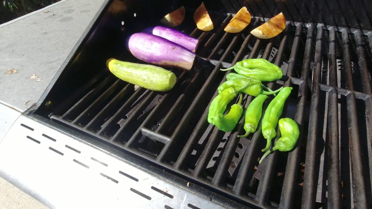 A close view into the Los Cabos grill shows purple eggplant and green peppers catching bright sun while browned wedges sit near the back, with no visible people.