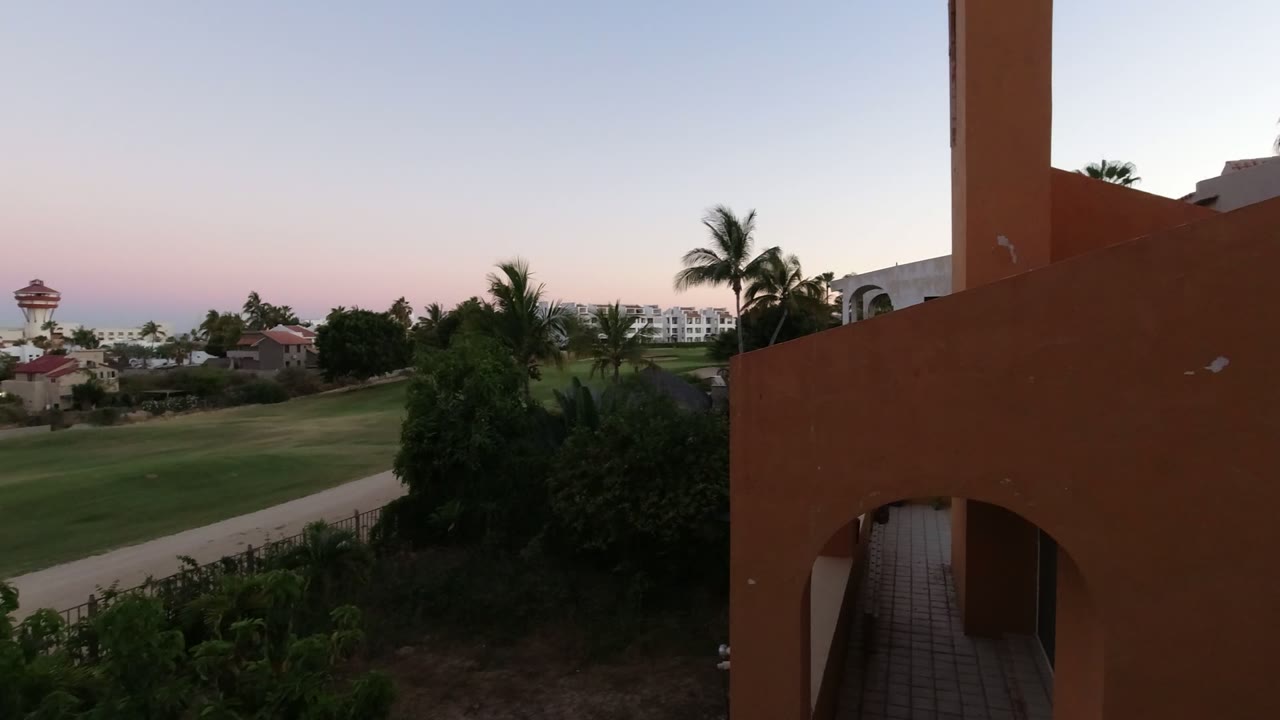 Orange building beside palms, lawn, and sunset sky