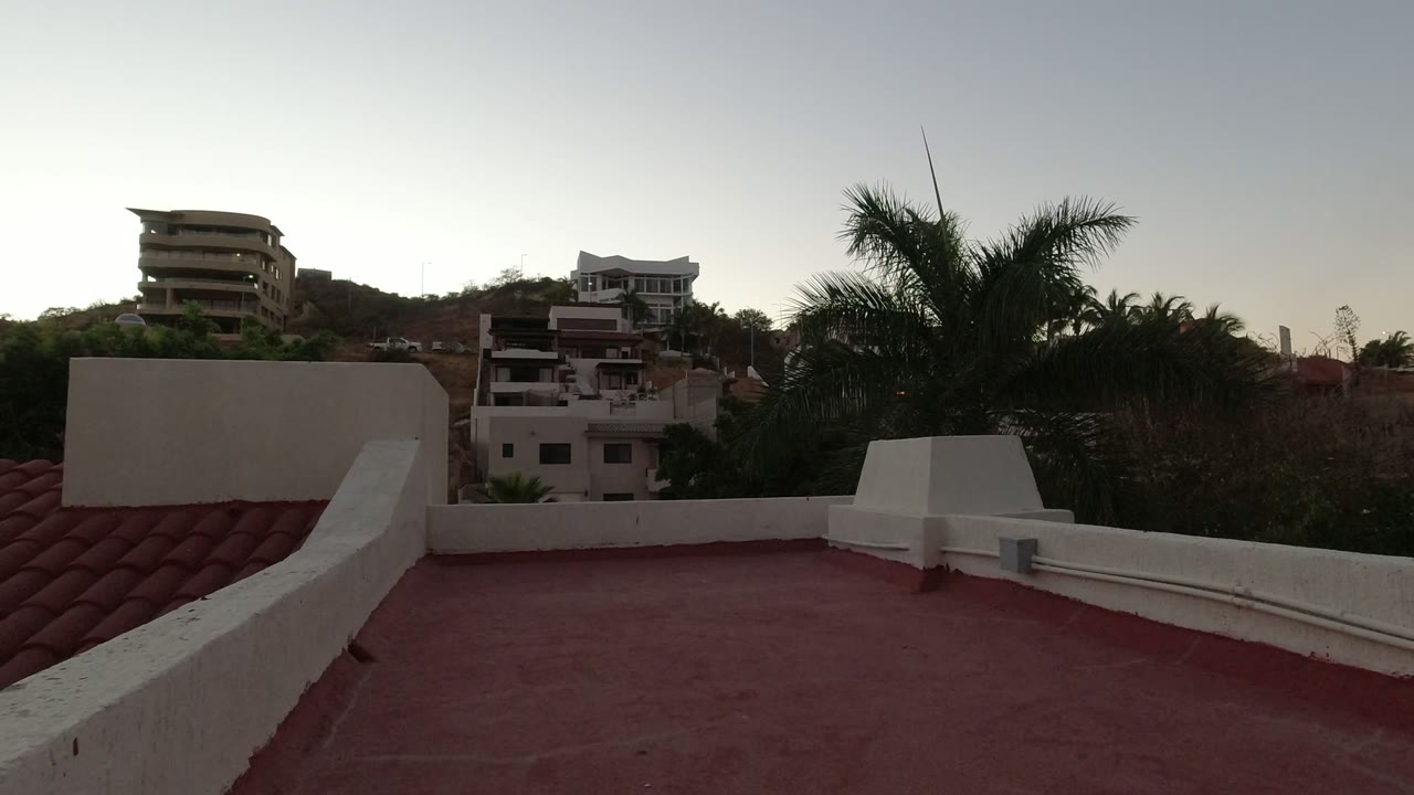 Second frame shows the Los Cabos roof edge and tile roof at left, with layered hillside buildings, palms, dry vegetation, and no visible people.