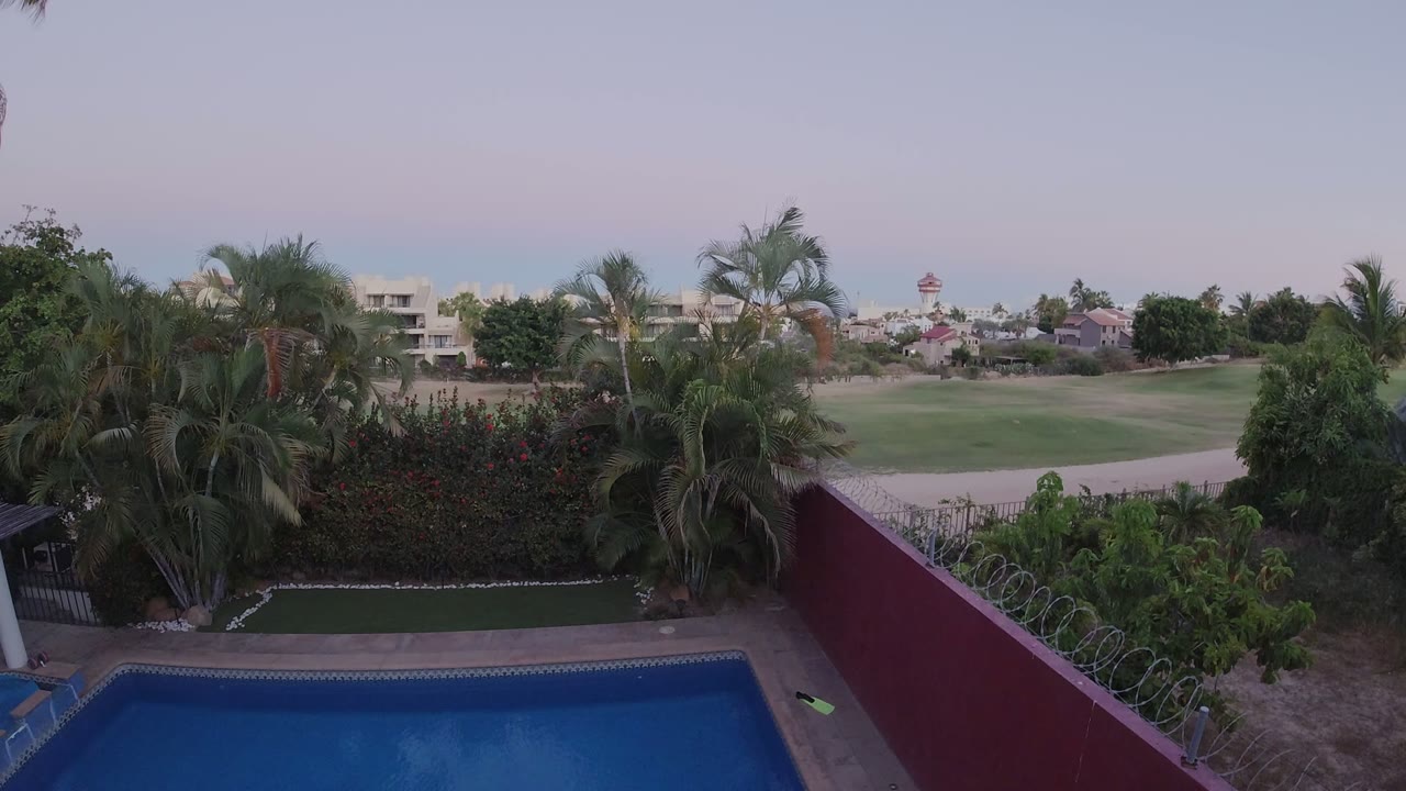 Elevated view of a private pool, red wall, palm trees, and green grounds beyond.