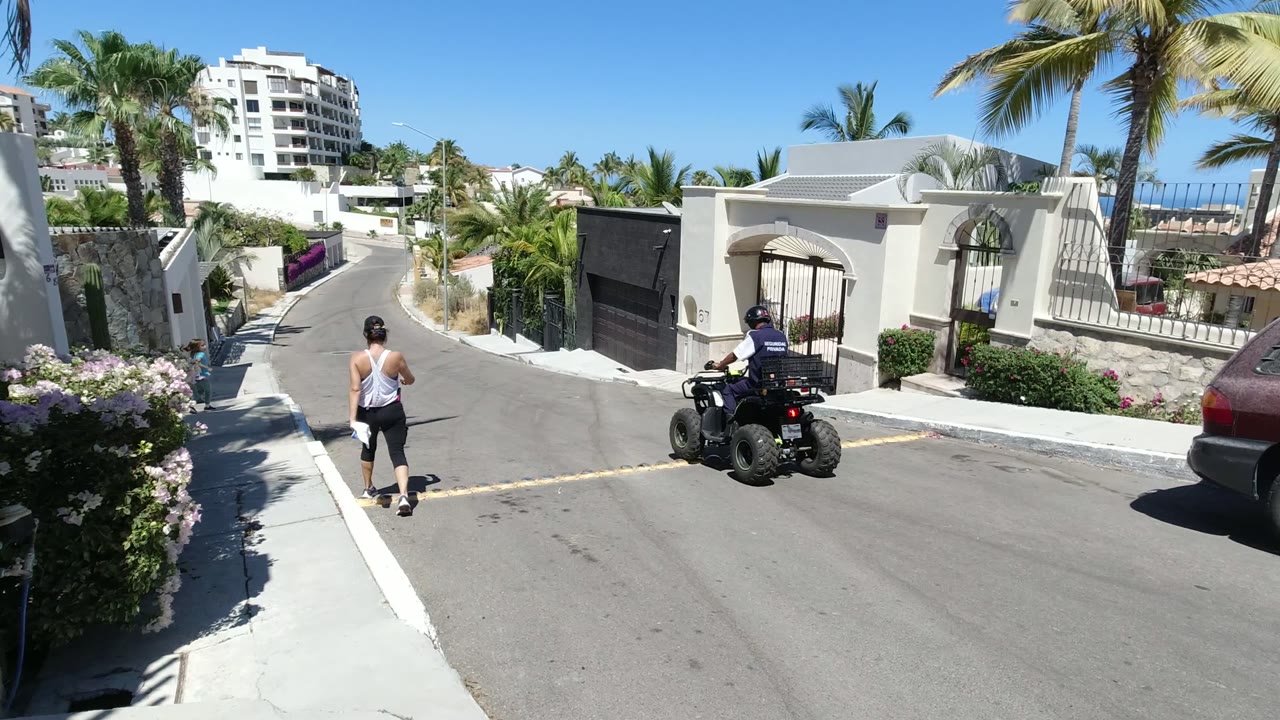 Sunny residential street with pedestrians and an ATV rider.