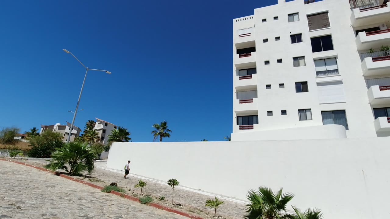 White building above a sidewalk with a man walking at the lower left.