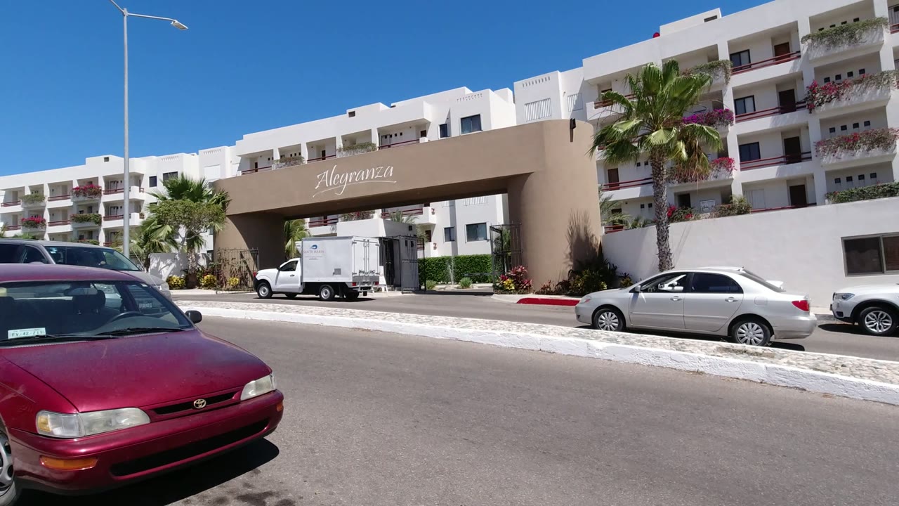 Sunny street outside a white hotel complex with a red car in the foreground.