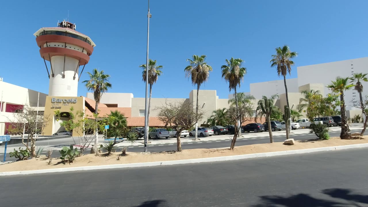 Second frame shows the Los Cabos exterior from a similar wide angle, with the tall tower left of center, palms across the lot, parked vehicles, and no visible people.