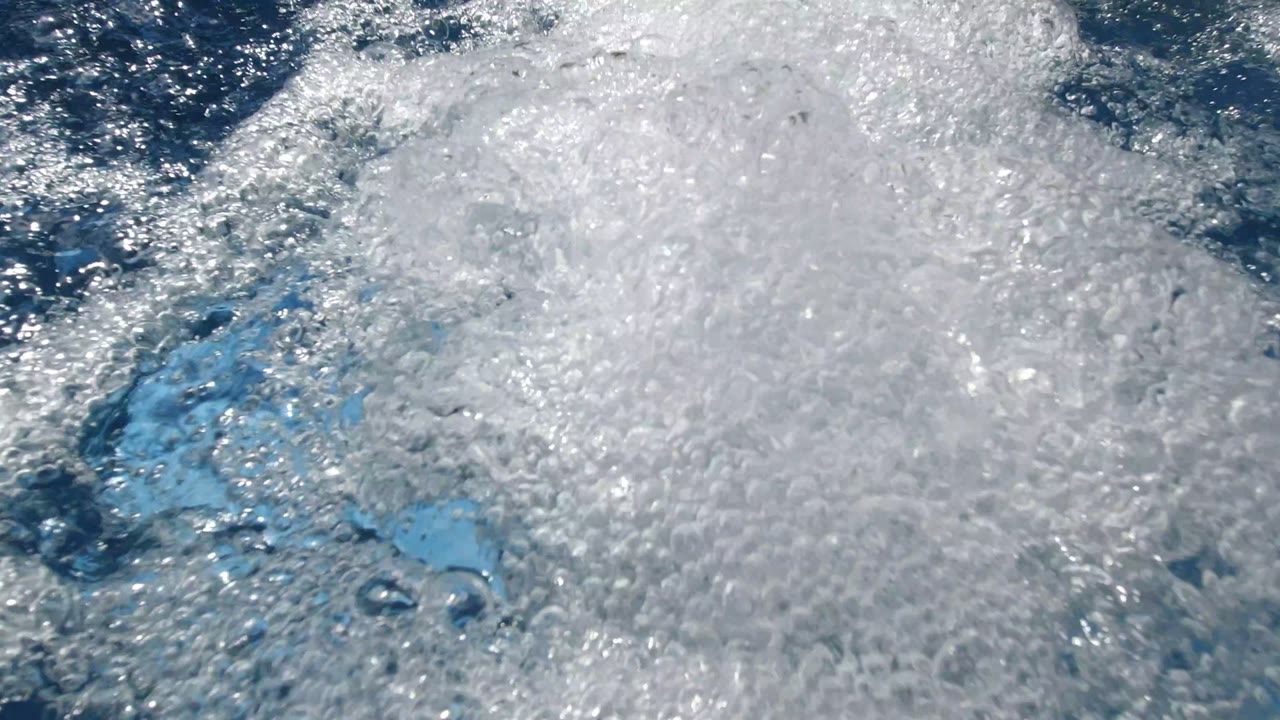 A dense cluster of white jacuzzi bubbles covers most of the frame while darker blue water breaks through in Los Cabos, Mexico, with no visible people.