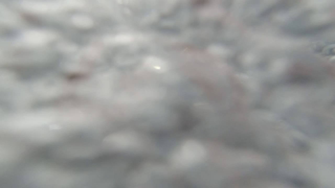 Soft close-up of pale foamy water texture from the Los Cabos Mexico clip, with blue-gray shadows and no visible people.
