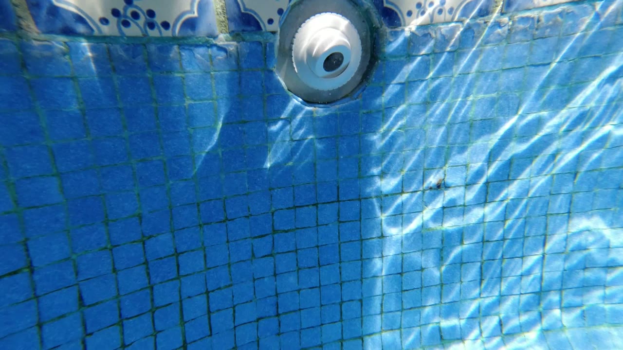 Blue tiled pool wall with rippled sunlight and a white circular inlet near the top.