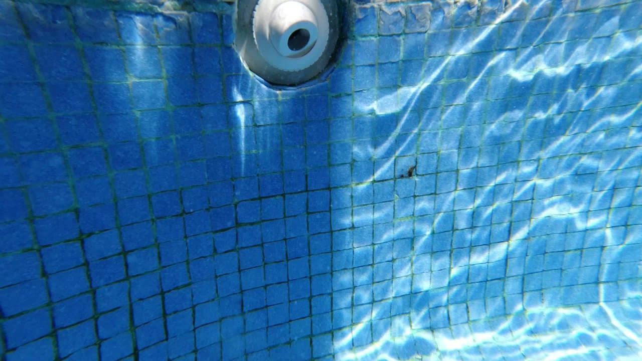 At 0:01, the Los Cabos pool wall remains tightly framed as brighter water reflections cross the blue tiles below the white inlet, with no visible people.