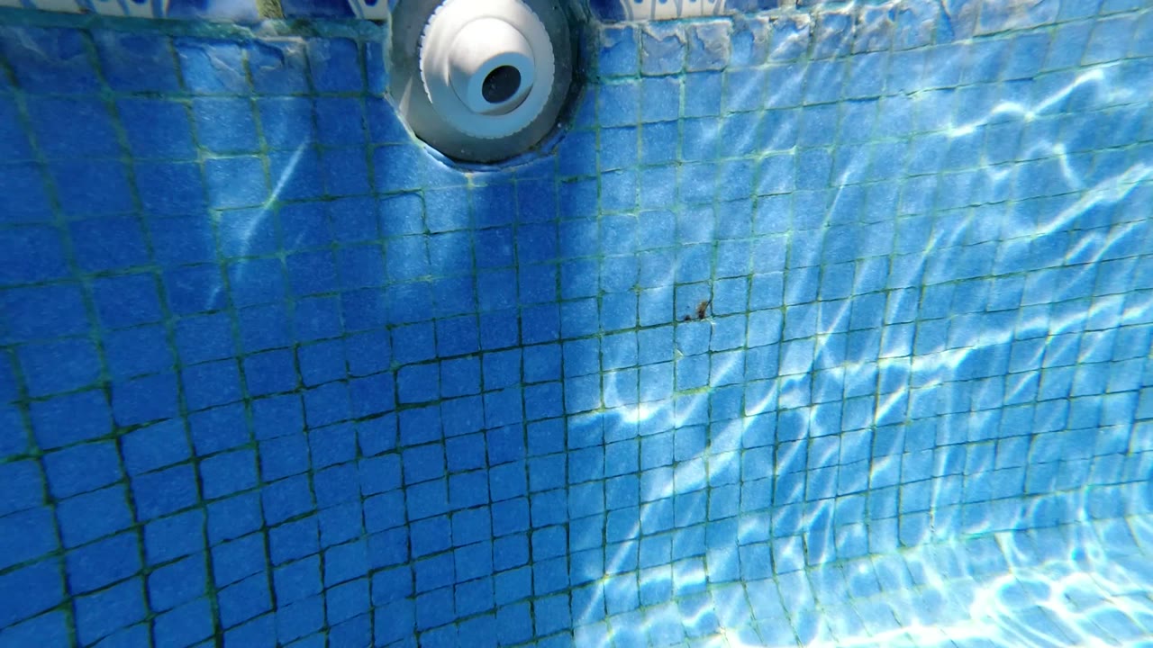 Start frame of a Los Cabos pool surface with blue square tile, a white circular jet near the top edge, bright water reflections, and no visible people.