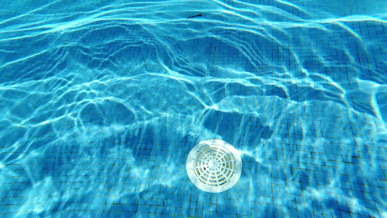 Pool water in Los Cabos, Mexico, shows shifting bright caustics across the tiled floor with a white drain near the middle, no visible people.