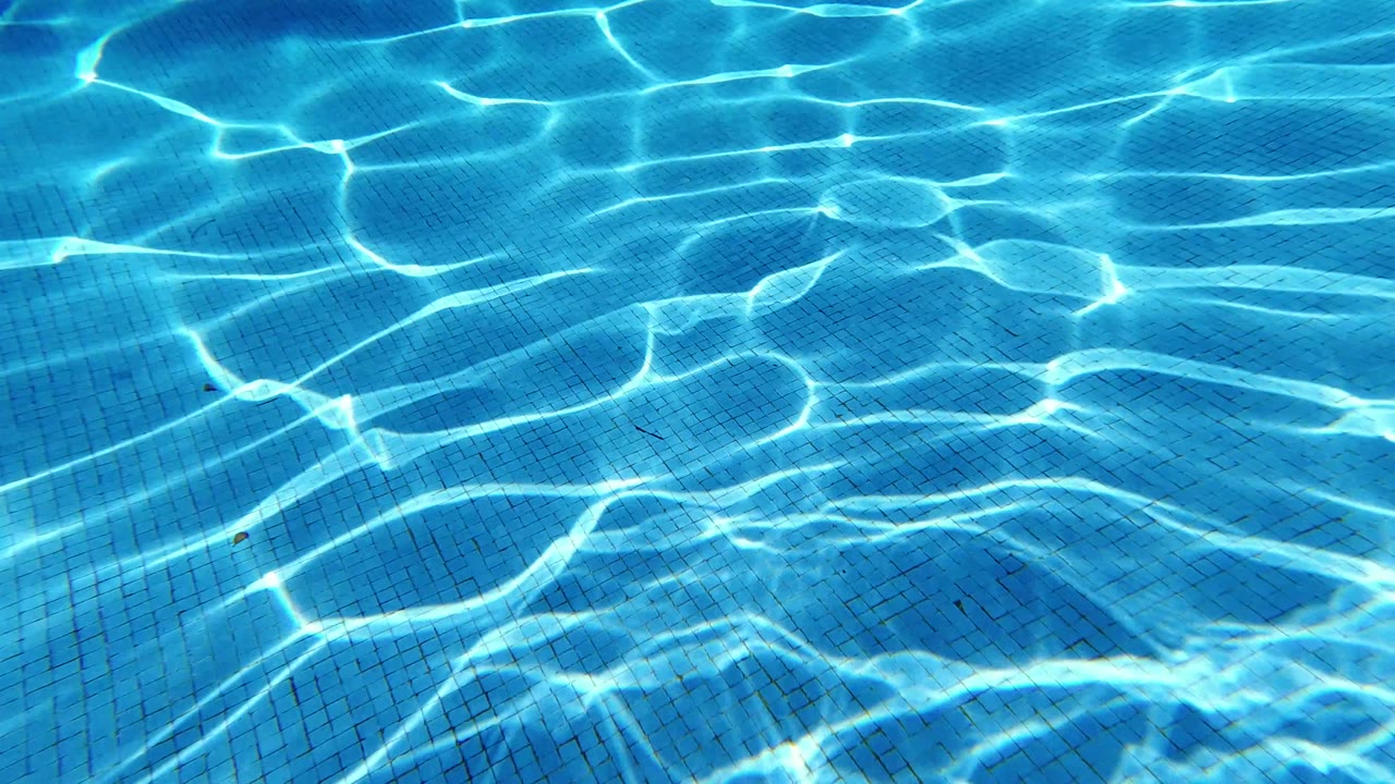 Clear blue pool water in Los Cabos fills the frame with tight tile lines and bright caustic light patterns, with no visible people.