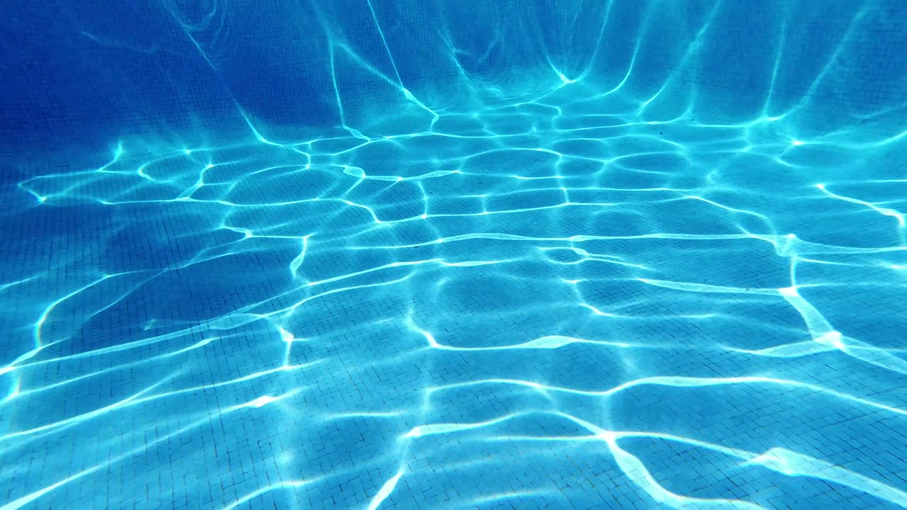 Blue pool water with sunlight ripples on the floor and wall.