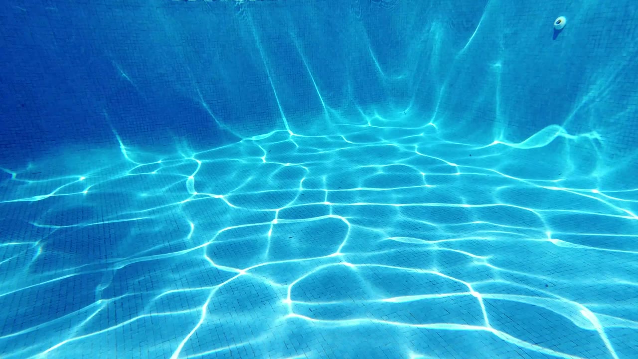 Clear underwater pool frame from Los Cabos, Mexico, with shifting bright lines across the blue floor and wall and no visible people.
